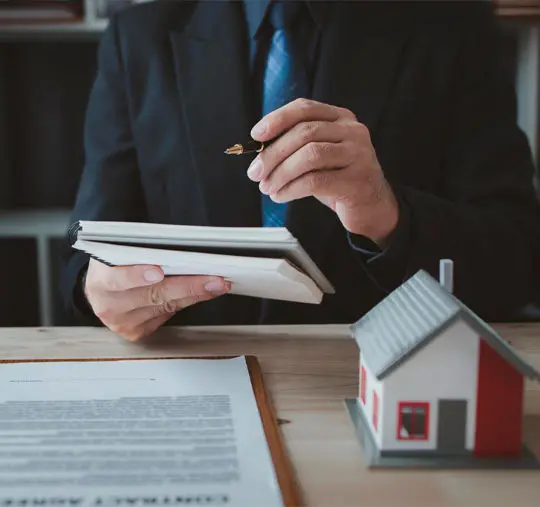 Advogado com contrato imobiliário e maquete de casa sobre a mesa de trabalho